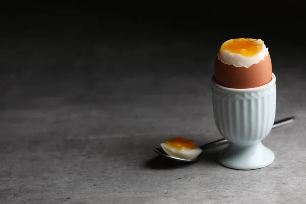 Cup with fresh soft boiled egg on grey table, space for text