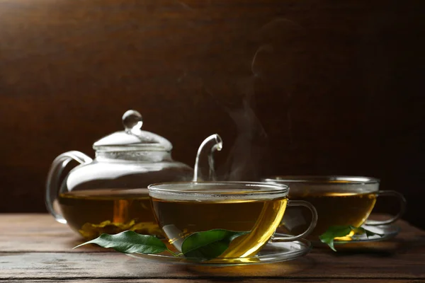 玻璃杯中的新鲜绿茶 木桌上的叶子和茶壶 — 图库照片