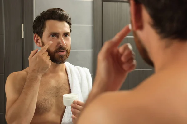 鏡の近くのバスルームで顔にクリームを適用ハンサムな男 — ストック写真