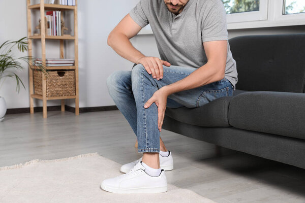 Мужчина, страдающий от боли в ноге на диване дома, крупным планом