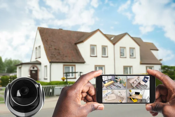 Home security system. African American man monitoring modern CCTV cameras on smartphone near his house, closeup