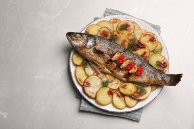 Açık gri masada lezzetli fırında levrek ve patates tabağı, üst manzara. Metin için boşluk