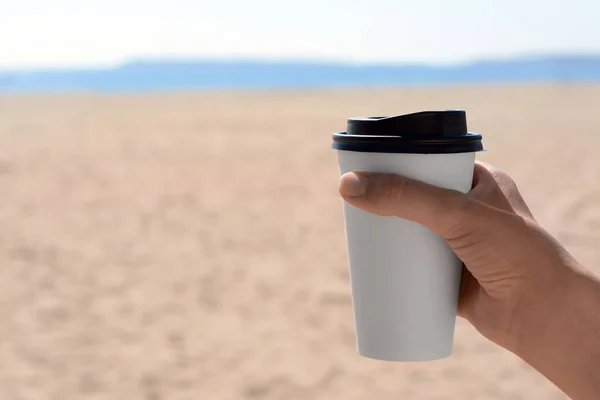 Woman with takeaway coffee cup on beach, closeup. Space for text