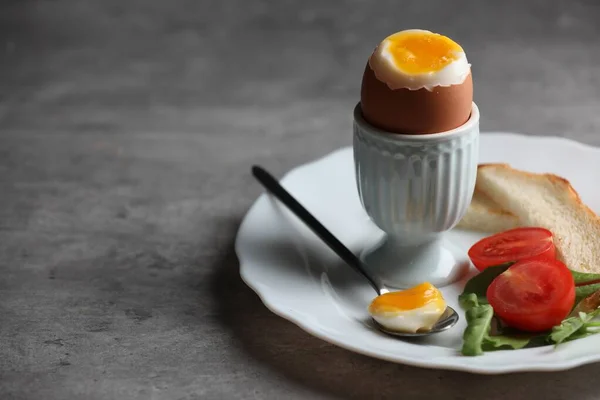 Delicious breakfast with soft boiled egg and fresh tomato served on grey table, closeup. Space for text