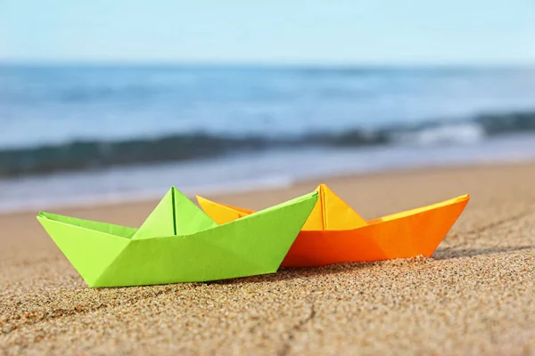 stock image Bright color paper boats on sandy beach near sea