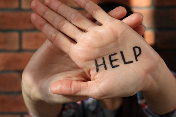Domestic violence concept. Woman hiding her face, focus on hands with written word Help