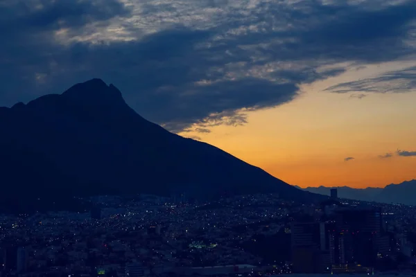 大きな山と夕方の都市の上に暗い雲と夕日の絵のような景色 — ストック写真