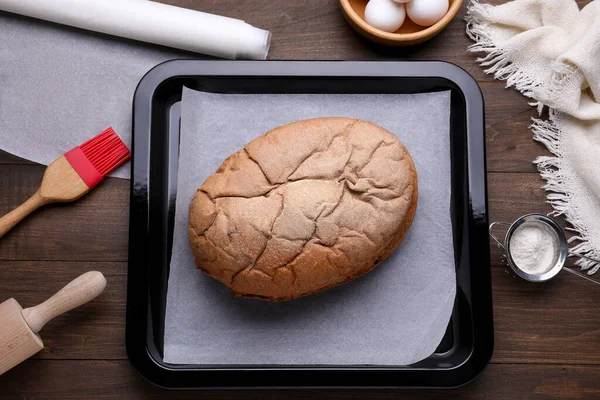 Baking pan with parchment paper and tasty homemade bread on wooden table, flat lay