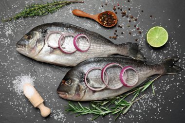 Düz kompozisyonda taze çiğ dorado balığı ve malzemeleri siyah masanın üzerinde duruyordu.