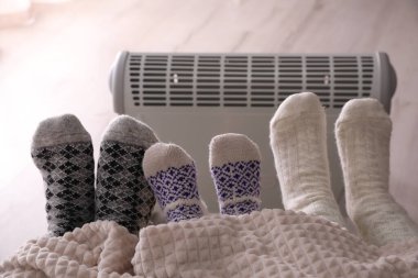 Evdeki elektrikli ısıtıcının yanında ayaklarını ısıtan aile, yakın çekim.