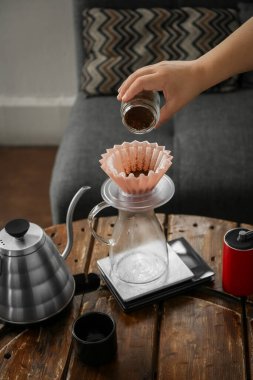 Barista kafedeki ahşap masada kahve ve damlatıcıyla sürahiye koyuyor, yakın plan.