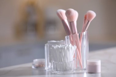 Pamuk tomurcukları, pedler ve makyaj fırçaları şeffaf tutacaklarda, aydınlık masada.