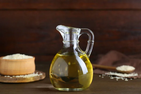 Jug of organic sesame oil and seeds on wooden table