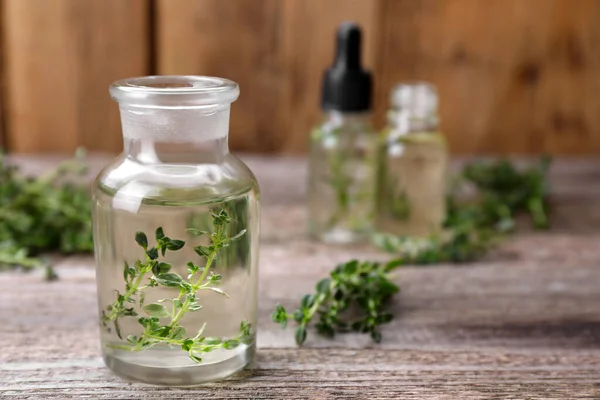 Thyme essential oil and fresh plant on wooden table, closeup. Space for text