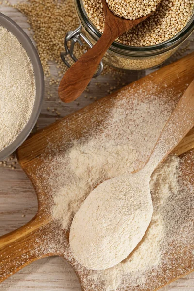 Spoon and bowl of quinoa flour near jar with seeds on wooden table, flat lay