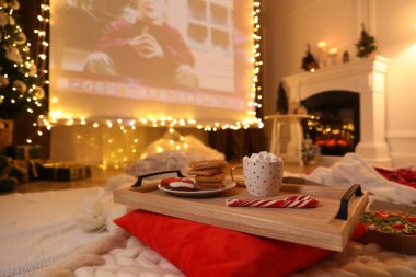 MYKOLAIV, UKRAINE - 24 Aralık 2020: Evde Tek Başına filmi odada gösteren video projektör ekranı, aperatif ve içkili tepsiye odaklanın. Sıcak kış tatili atmosferi