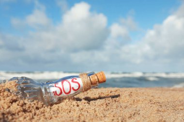 Deniz kenarındaki kumda SOS mesajı olan cam şişe, metin için boşluk