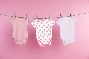 Bebek tulumları pembe arka planda çamaşır ipinde kuruyor.