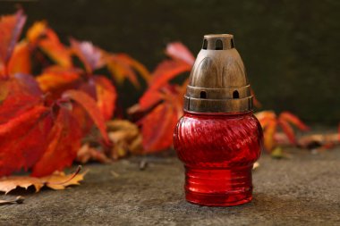 Mezarlıktaki taş yüzeyde kırmızı mezar feneri ve düşen yapraklar, metin için alan