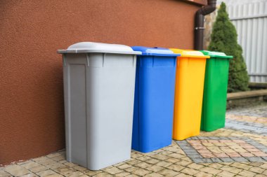 Açık havada kahverengi duvarın yanında birçok renk geri dönüşüm kutusu var.