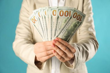 Turkuaz arka planda dolar banknotları tutan kadın, yakın plan. Para değişimi kavramı