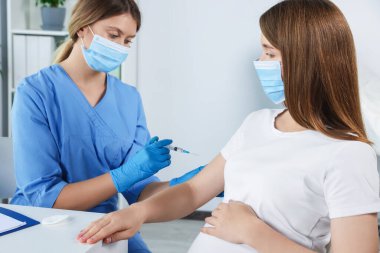 Doktor hastanede hamile kadına iğne yapıyor.