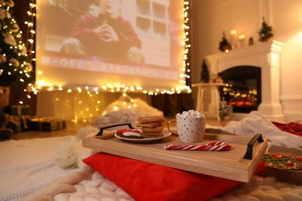 MYKOLAIV, UKRAINE - DECEMBER 24, 2020: Video projector screen displaying Home Alone movie in room, focus on tray with snack and drink. Cozy winter holidays atmosphere