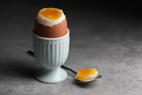 Cup with fresh soft boiled egg on grey table, closeup. Space for text