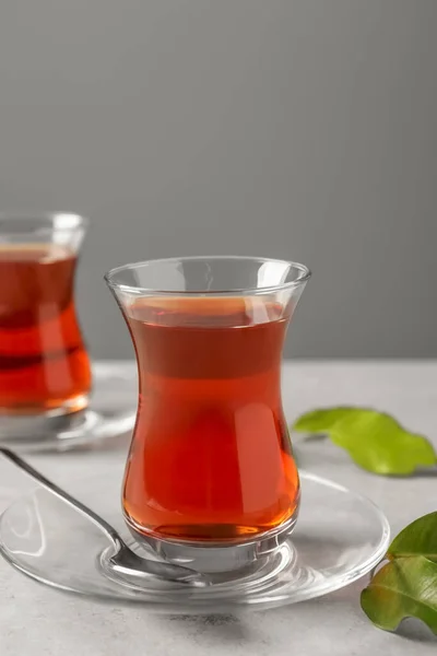 Glasses with traditional Turkish tea and green leaves on light grey table