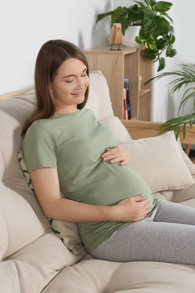 Szczęśliwa Kobieta Ciąży Siedzi Kanapie Dotyka Brzucha Salonie — Zdjęcie stockowe
