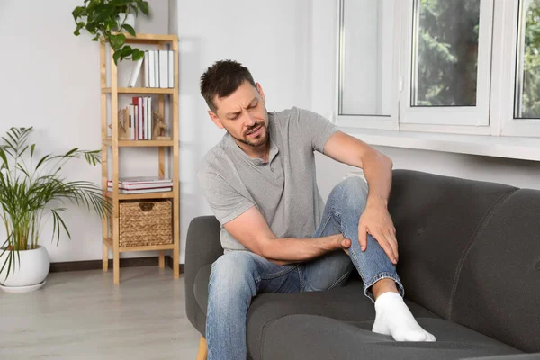 自宅でソファの上で足の痛みに苦しんでいる男 — ストック写真
