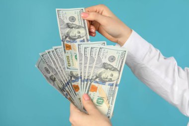 Turkuaz arka planda dolar banknotları tutan kadın, yakın plan. Para değişimi kavramı