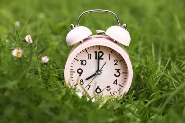 Yeşil çimlerin üzerindeki pembe alarm saati, yakın plan.