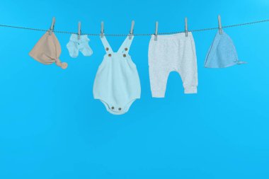 Çamaşır ipinde açık mavi arka planda farklı bebek kıyafetleri kurutuluyor.