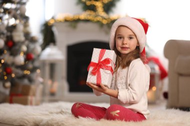 Noel için dekore edilmiş küçük şirin bir kız hediye kutusunu odada tutuyor.