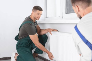 Professional plumbers installing new heating radiator in room
