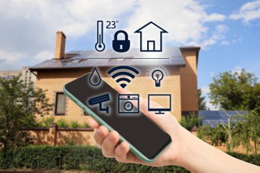 Açık havada akıllı evleri kontrol etmek için telefon uygulaması kullanan bir kadın.