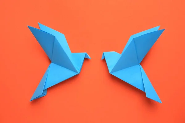 Beautiful light blue origami birds on orange background, flat lay
