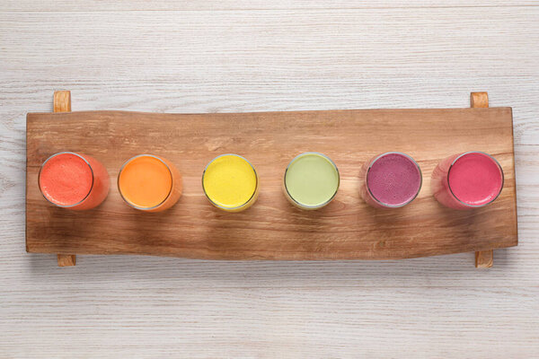 Board with many different tasty smoothies on white wooden table, top view