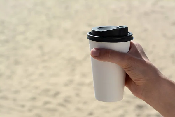 Woman with takeaway coffee cup on beach, closeup. Space for text