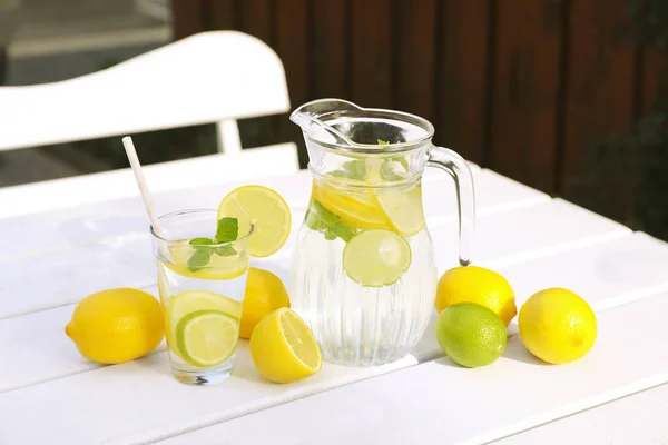 屋外の白い木製のテーブルの上にレモンと手足のある水 — ストック写真