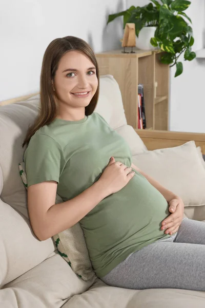 幸せな妊娠中の女性座っていますソファとタッチ彼女の腹でリビングルーム — ストック写真
