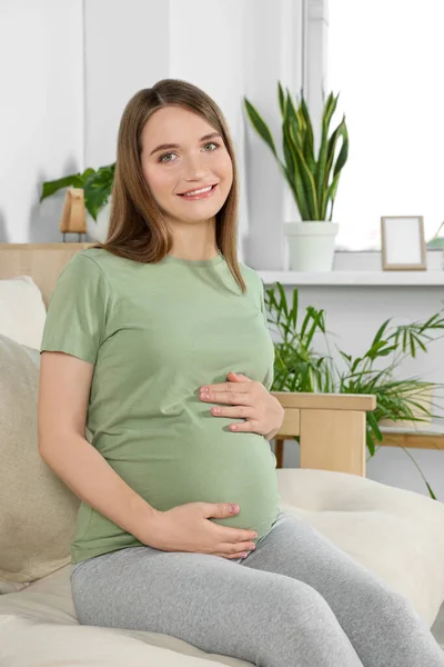 幸せな妊娠中の女性座っていますソファとタッチ彼女の腹でリビングルーム — ストック写真