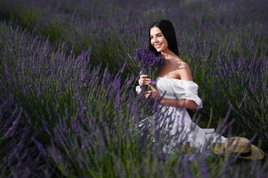 Beautiful young woman with bouquet sitting in lavender field