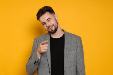 Gri ceketli yakışıklı adam sarı arka planda bir şeyi işaret ediyor.