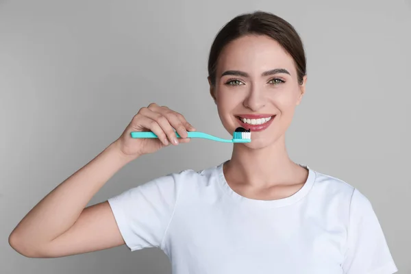 stock image Young woman holding toothbrush with charcoal toothpaste on grey background