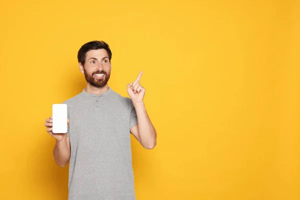 stock image Happy man with smartphone pointing at something on yellow background. Space for text