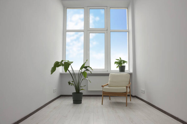 Empty renovated room with potted houseplants, armchair and windows