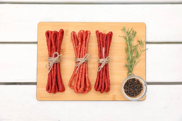 Stock image Bundles of delicious kabanosy with peppercorn and rosemary on white wooden table, top view