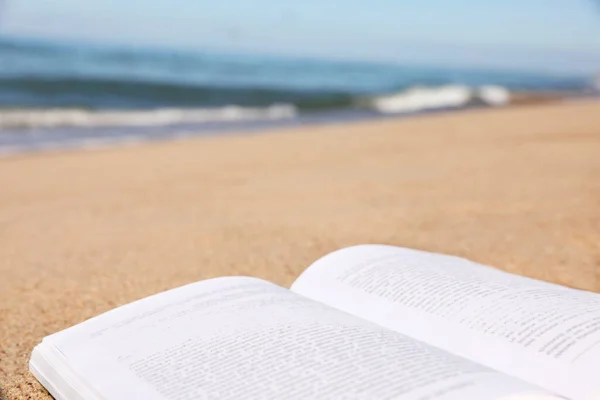 stock image Open book on sandy beach near sea, closeup. Space for text